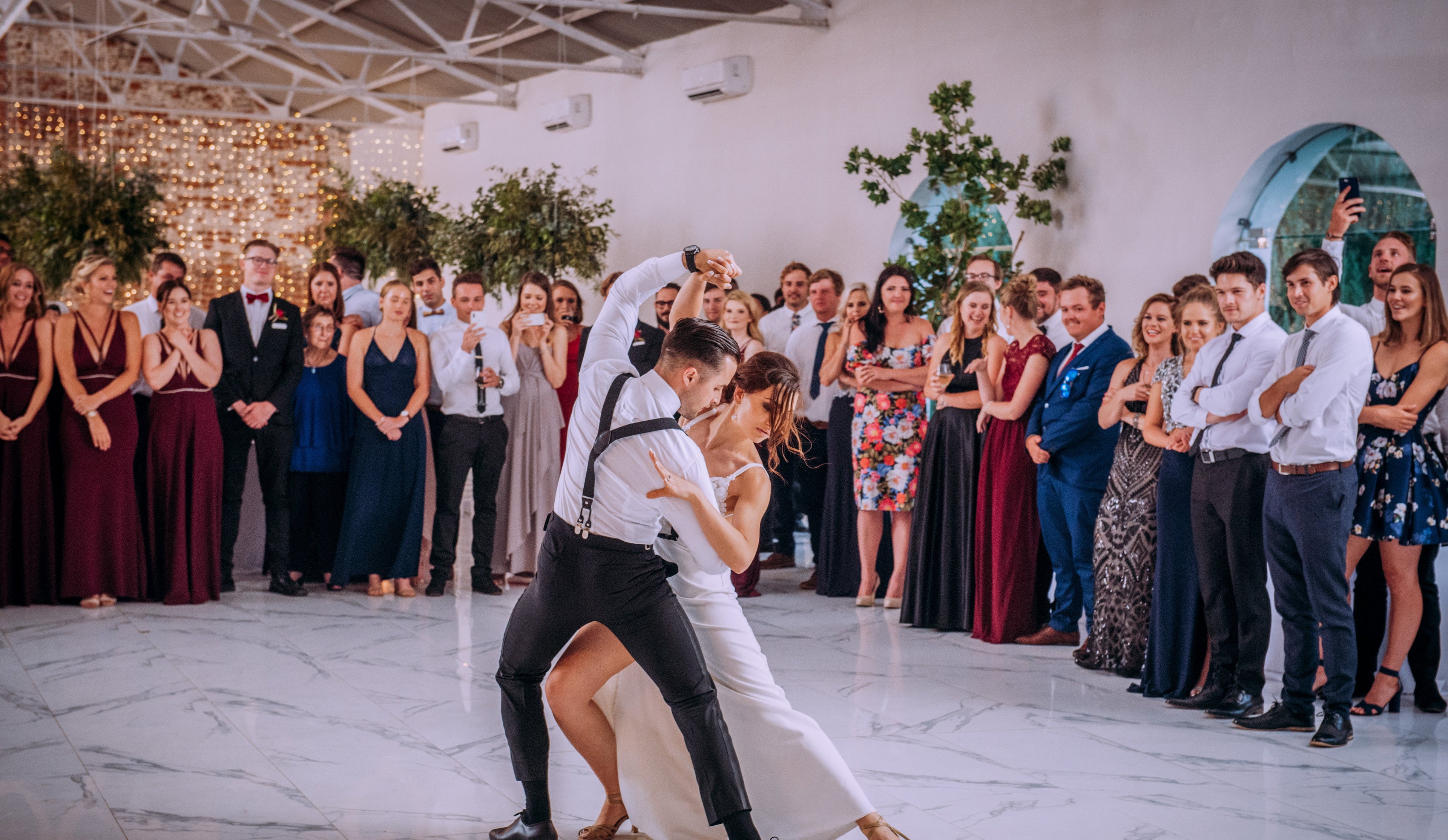 Couple dancing in the center of a room with guests watching, Shireen Louw Photography watermark.